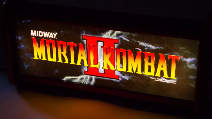 A lit Mortal Kombat 2 arcade marquee in the dark.