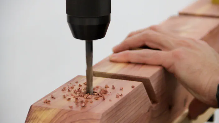 A drill press is used to drill a hole in a cedar skateboard rack.