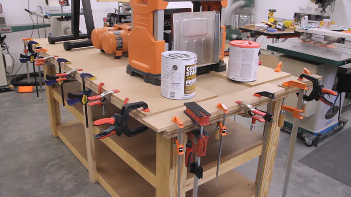 A piece of MDF is clamped to another using several clamps and weighted down.