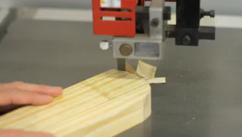 A piece of wood is cut at a bandsaw.