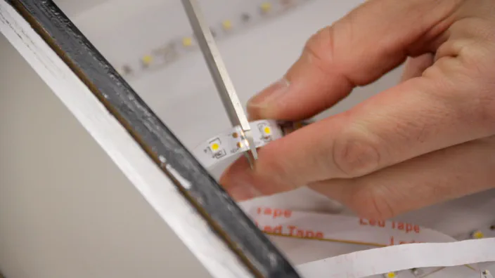 A LED light strip is cut with a pair of scissors.