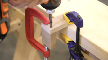 A drill is used to screw two small pieces of MDF together in an L shape.