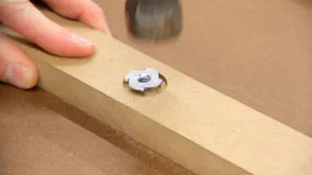 A T-nut is hammered into a piece of MDF.