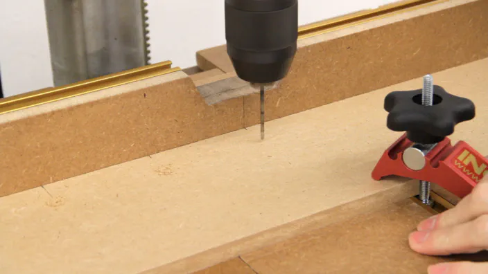 A drill press is used to drill several small holes in a piece of MDF.