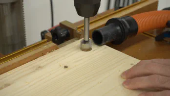 A drill press is used to drill a hole in wooden shelving.