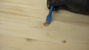 Glue and sawdust are used to fill in a crack in wooden shelving.