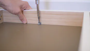 A screwdriver is used to attach the frame to the shelf top.