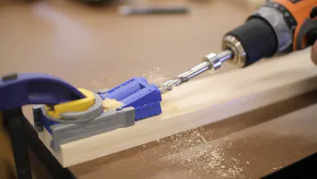 A pocket-hole jig is used to drill holes in a wooden board.