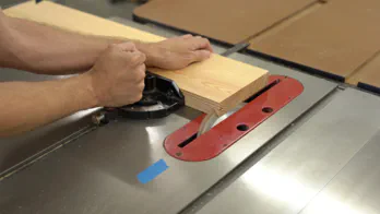 A table saw cuts the end of a board at a 45 degree angle.