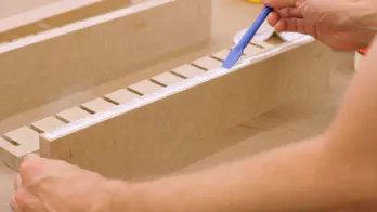 Glue is applied to the edge of a piece of MDF.