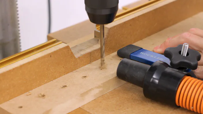 A drill press is used to drill holes in a piece of MDF.