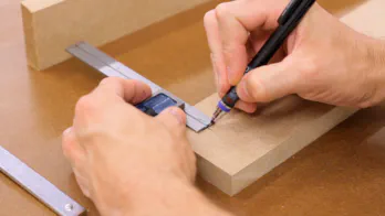 A pencil and square are used to mark on a piece of MDF.