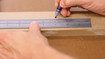 A pencil and ruler are used to mark on a piece of MDF.