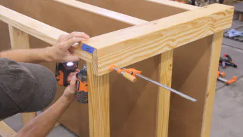 A drill is used to screw the workbench leg to the top frame.