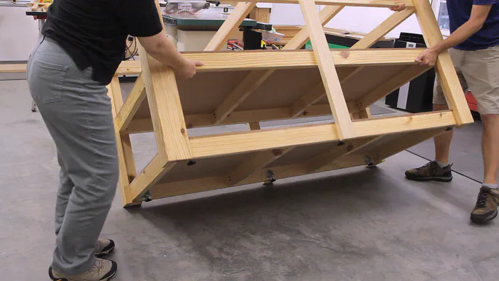 A workbench frame is carefully turned upright.