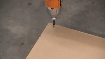 A drill is used to insert a screw into a piece of MDF.