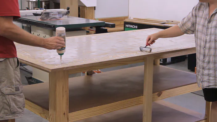 Glue is spread with a roller on an MDF table top.