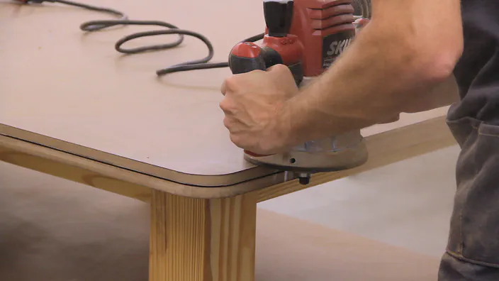 A router is used to cut a slot on the edge of a workbench top.