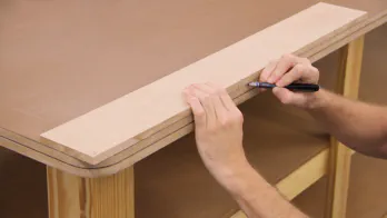 A pencil is used to transfer marks from a piece of MDF to a workbench top.