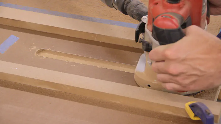 A router is used to cut a slot on the edge of a workbench top.
