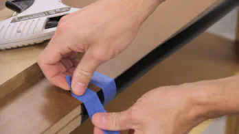 Blue painters tape is used to secure the T-molding onto the edge of the workbench top.