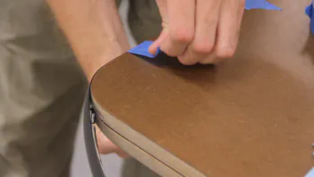 Blue painters tape is used to secure the T-molding onto the edge of the workbench top.