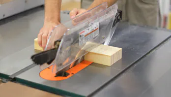A piece of wood is cut at a table saw.