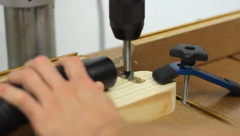 A drill press is used to drill partial holes in a piece of wood.